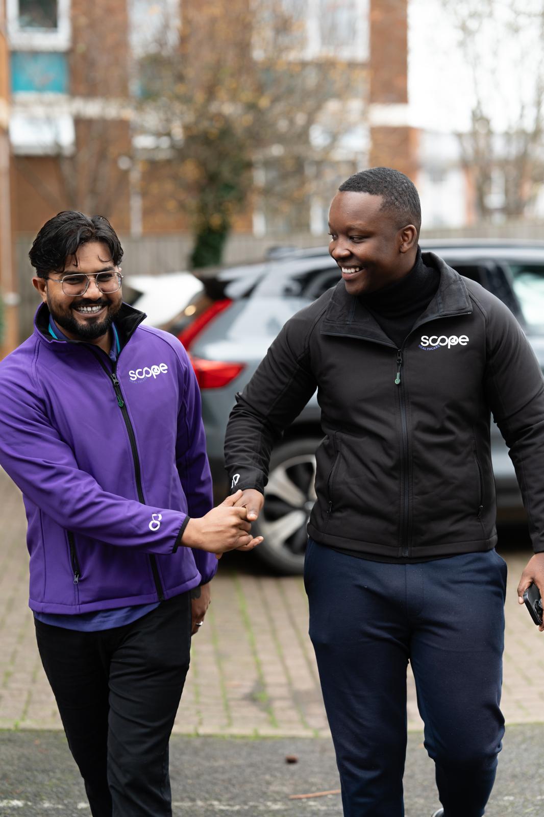 Two Scope Care team members smiling and shaking hands outside